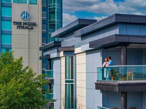 A modern hotel building with a prominent sign, a balcony with a glass railing, and a clear sky in the background. - Hotel Ithaca (Ithaca)