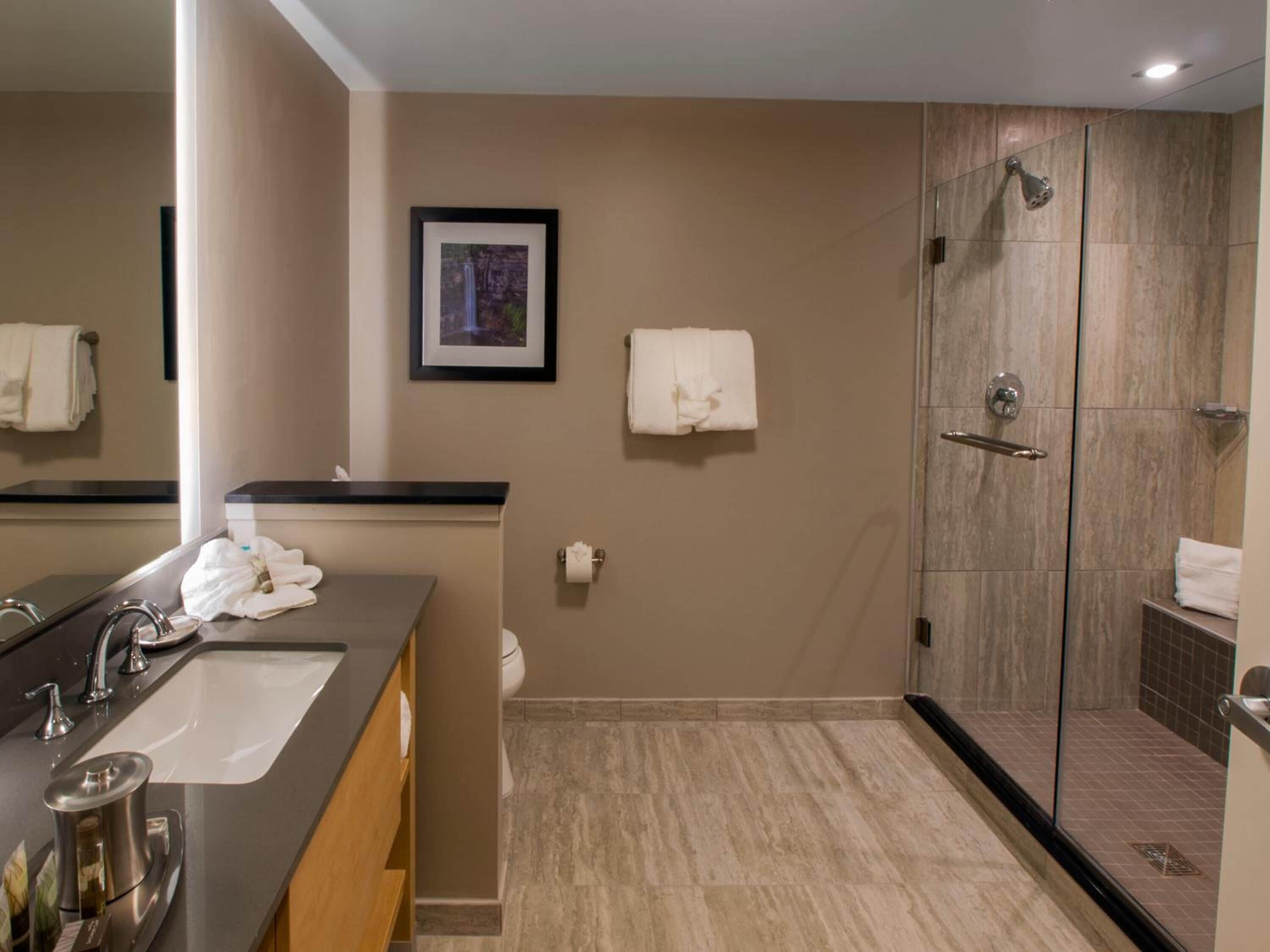 A modern bathroom with a sink, mirror, towel rack, shower, and a framed picture on the wall.