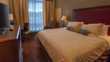 A hotel room with a large bed, a desk with a TV, a chair, and a window with curtains.