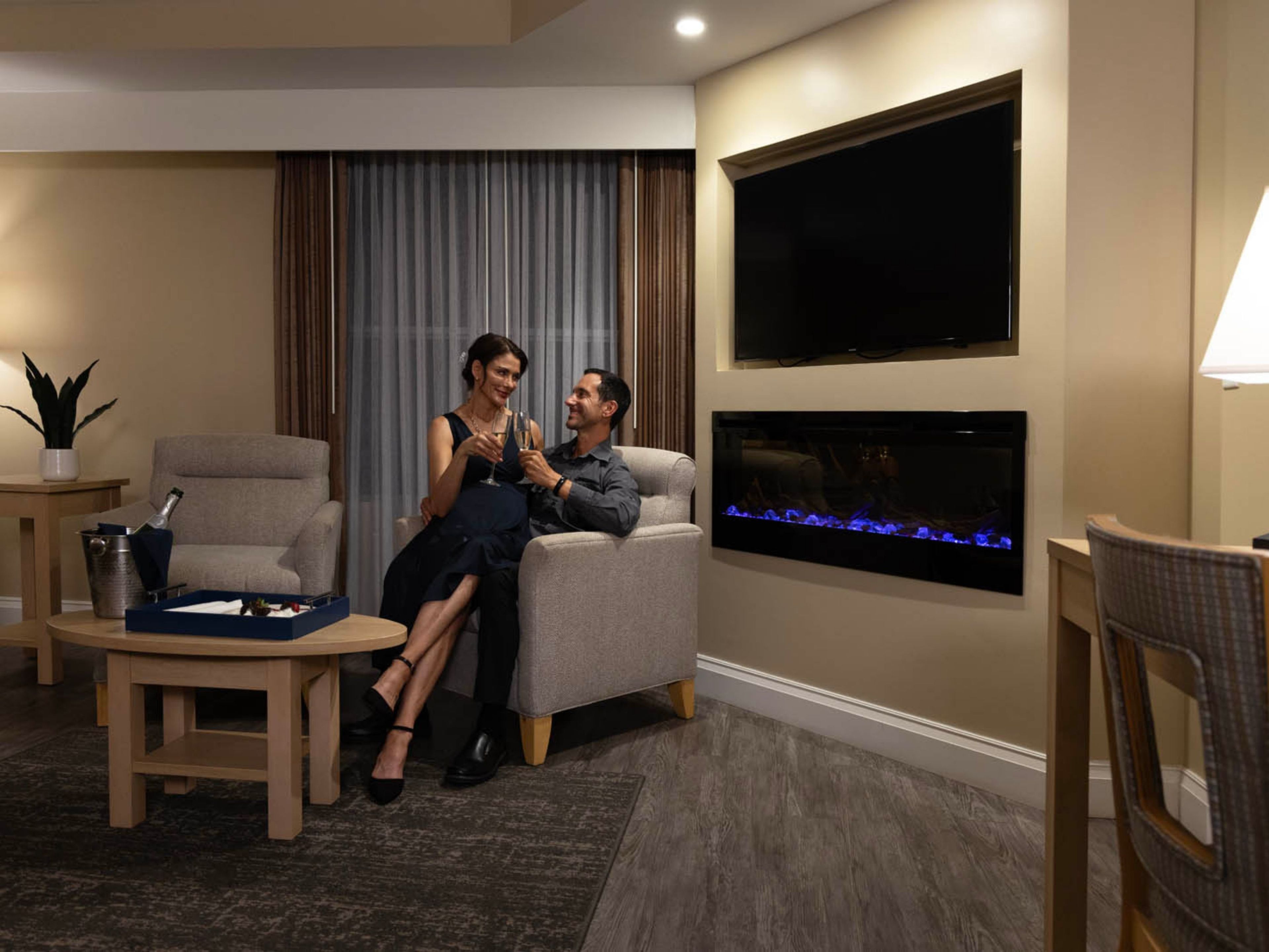A modern living room with a flat-screen TV, a fireplace, and a dining area with a table and chairs.