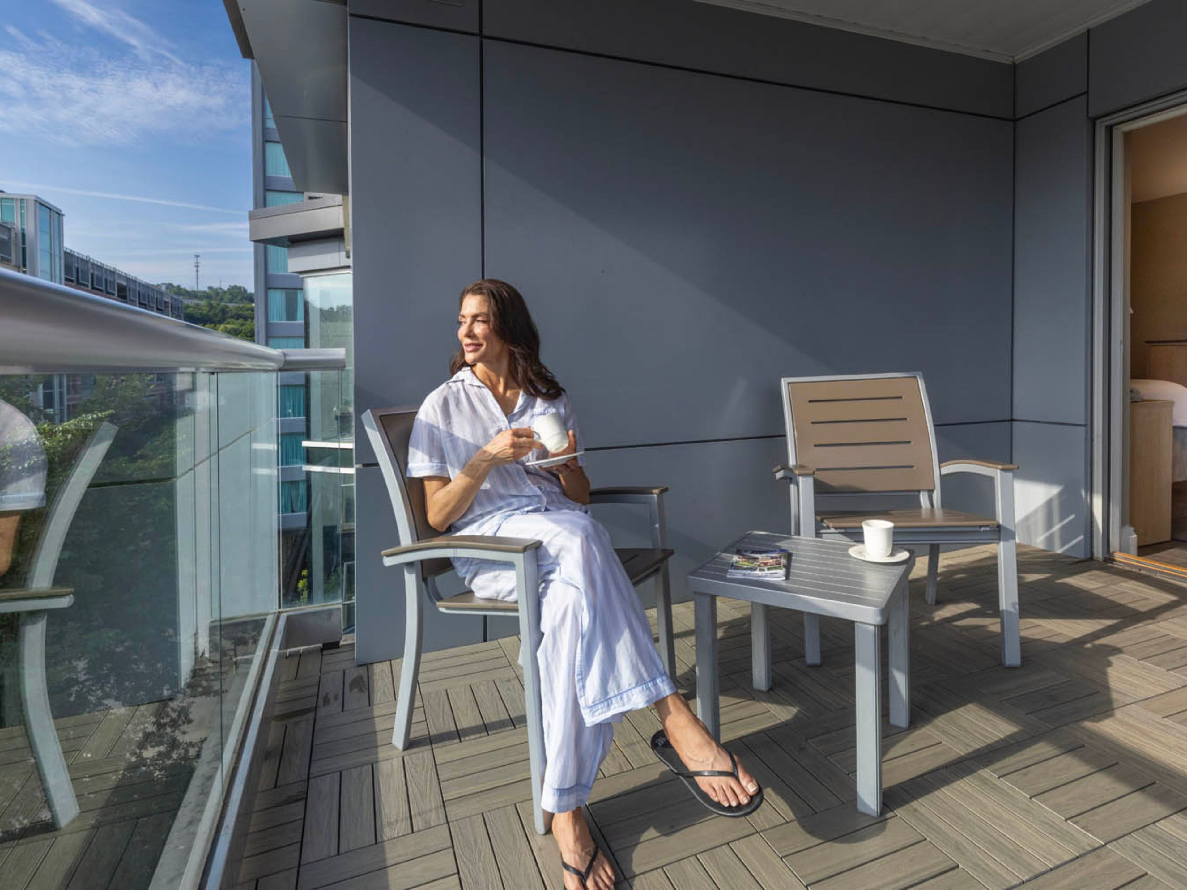 A balcony with a person seated on a chair, a table with a magazine, and another chair.