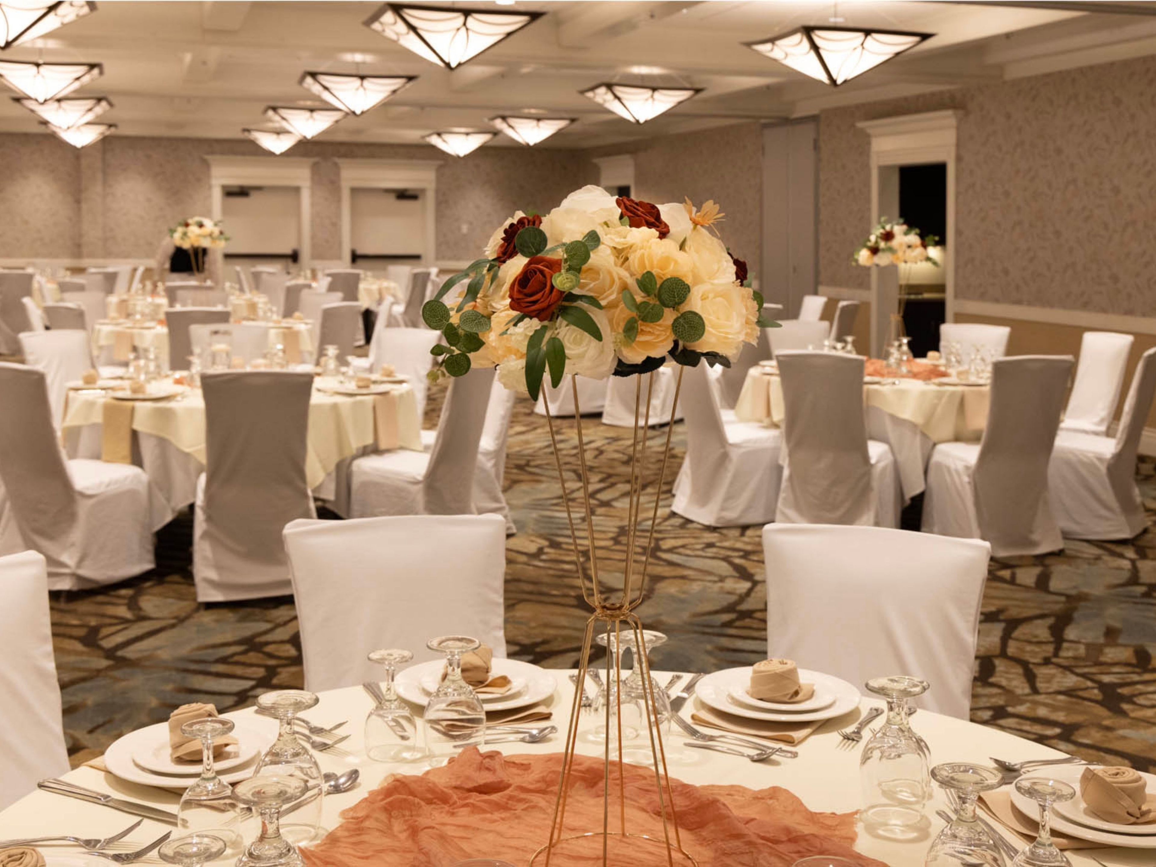Un salón de banquetes con mesas redondas dispuestas para cenar, cada una con manteles blancos, sillas y copas.