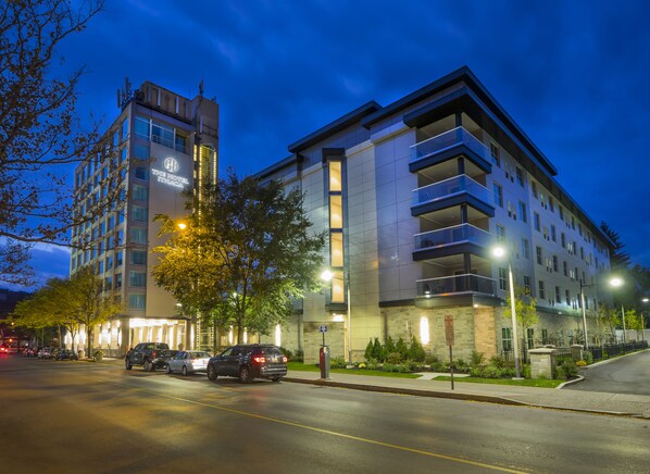 A multi-story hotel with a modern design, featuring balconies on the upper floors and a well-lit facade.