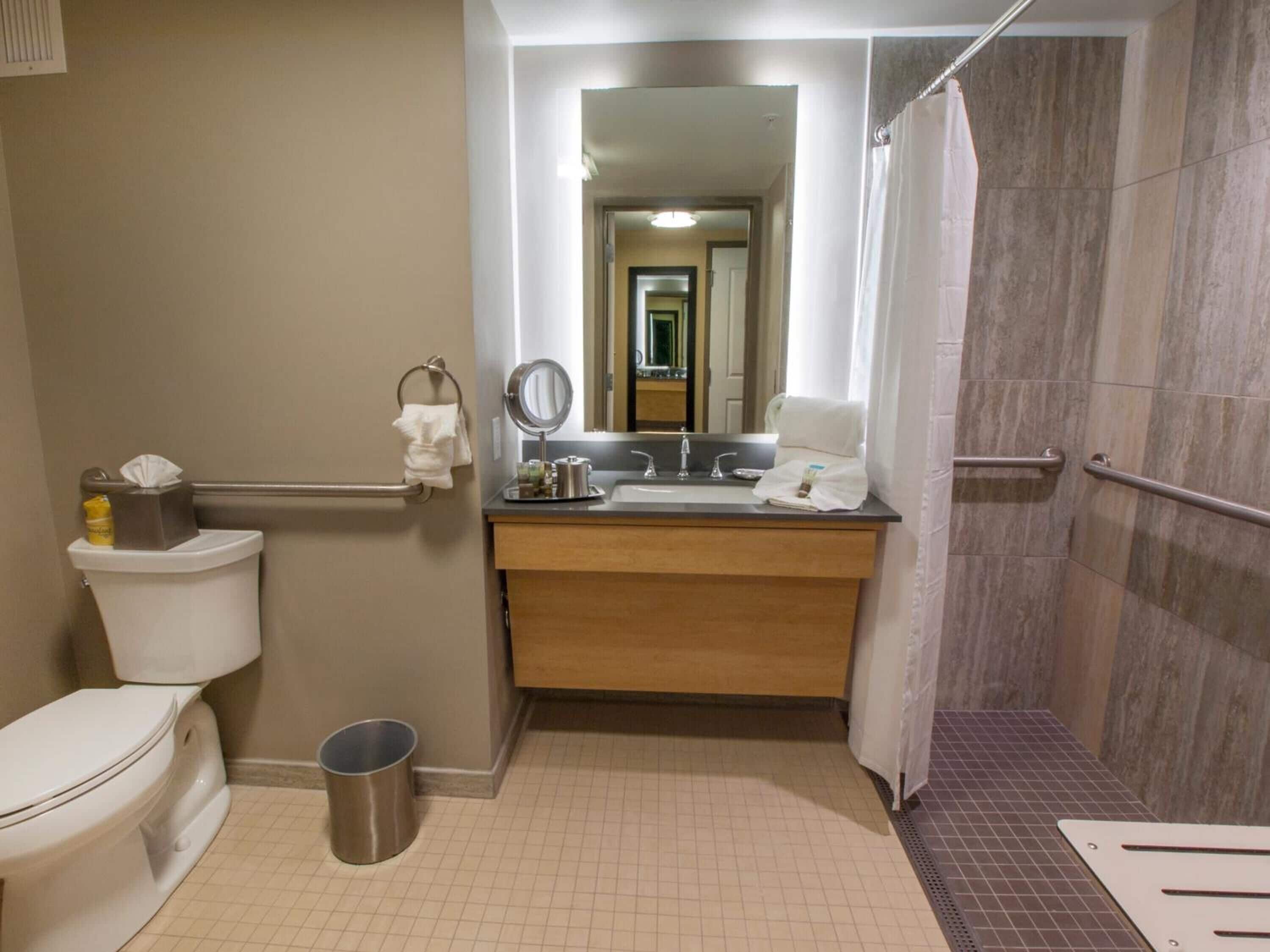 Et standard badeværelse med toilet, vask, spejl og bruser.