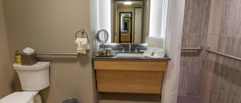 Et standard badeværelse med toilet, vask, spejl og bruser.
