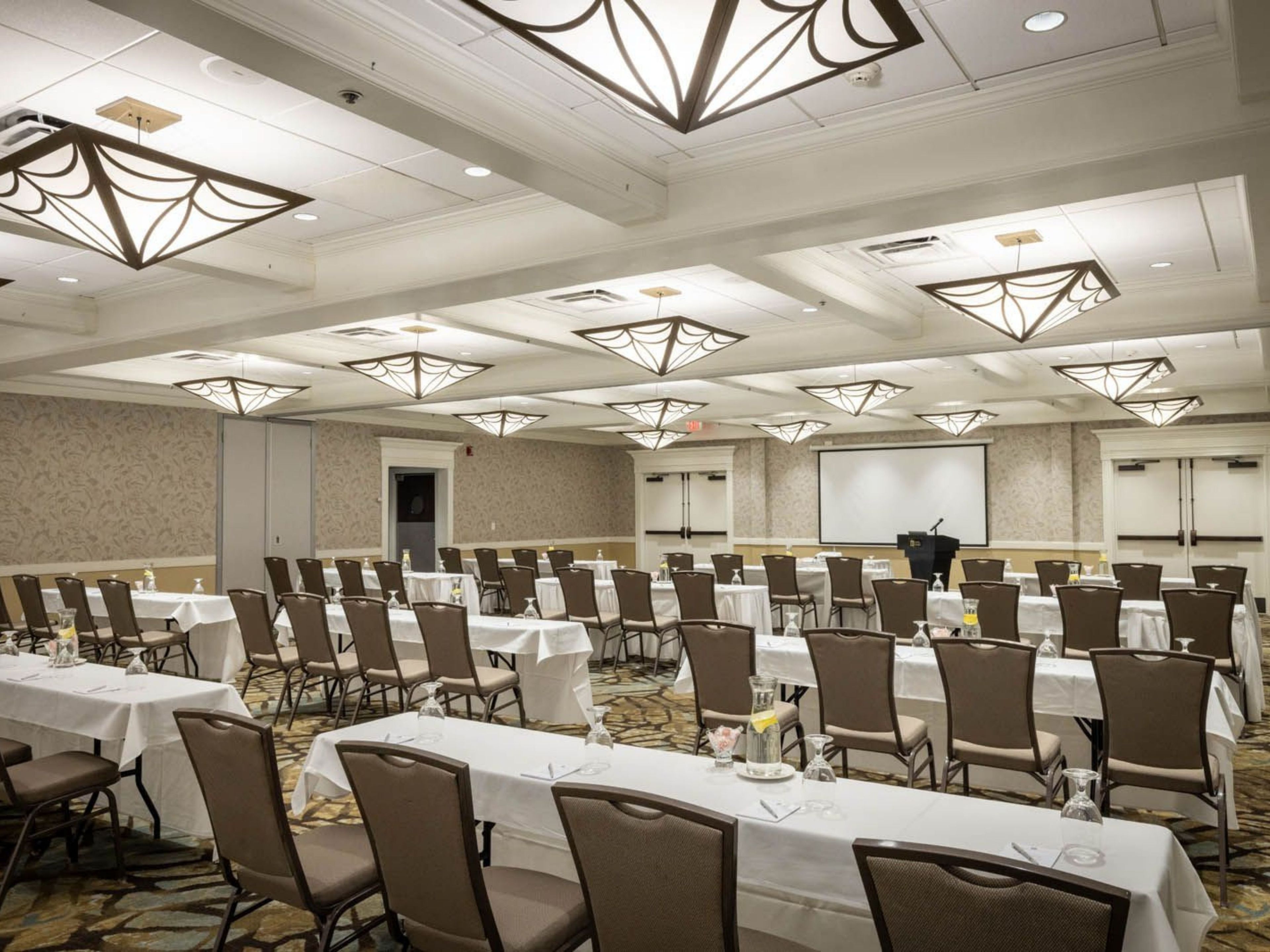 A conference room with multiple tables and chairs, a projector screen, and a speaker's podium.
