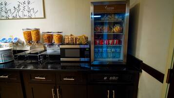 A breakfast bar with a coffee machine, a refrigerator stocked with beverages, and a food display.