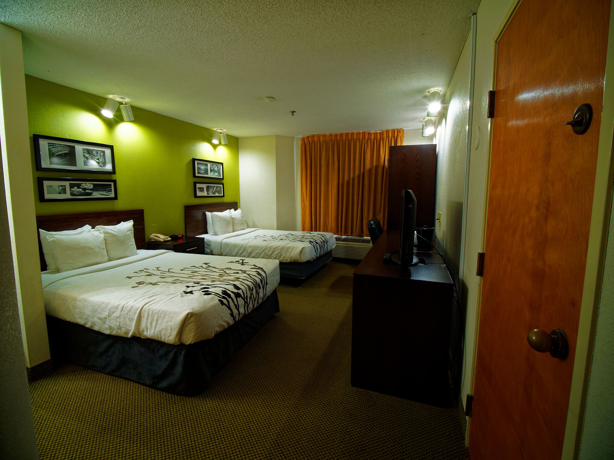 A hotel room with two beds, a desk, a television, and a door.