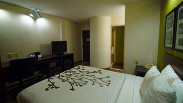 A hotel room with a bed, a television on a desk, a telephone, and a door leading to a bathroom.