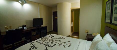 Ett hotellrum med en säng, en tv på ett skrivbord, en telefon och en dörr som leder till ett badrum.