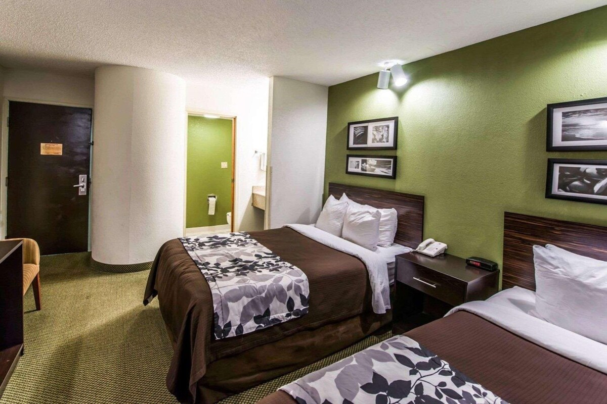 Een hotelkamer met twee bedden, een bureau met telefoon en een groene muur met ingelijste foto's.