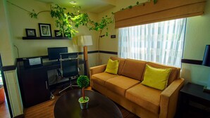 Un salon confortable avec un canapé, une table basse, un bureau avec un ordinateur et une fenêtre équipée de stores.