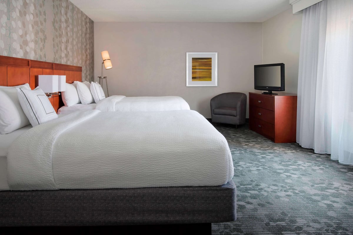 Een hotelkamer met een groot bed, een bureau met een televisie, een stoel en een lamp.
