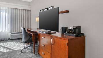 Quarto de hotel com escrivaninha de madeira, televisão de tela plana, cafeteira e uma cadeira.