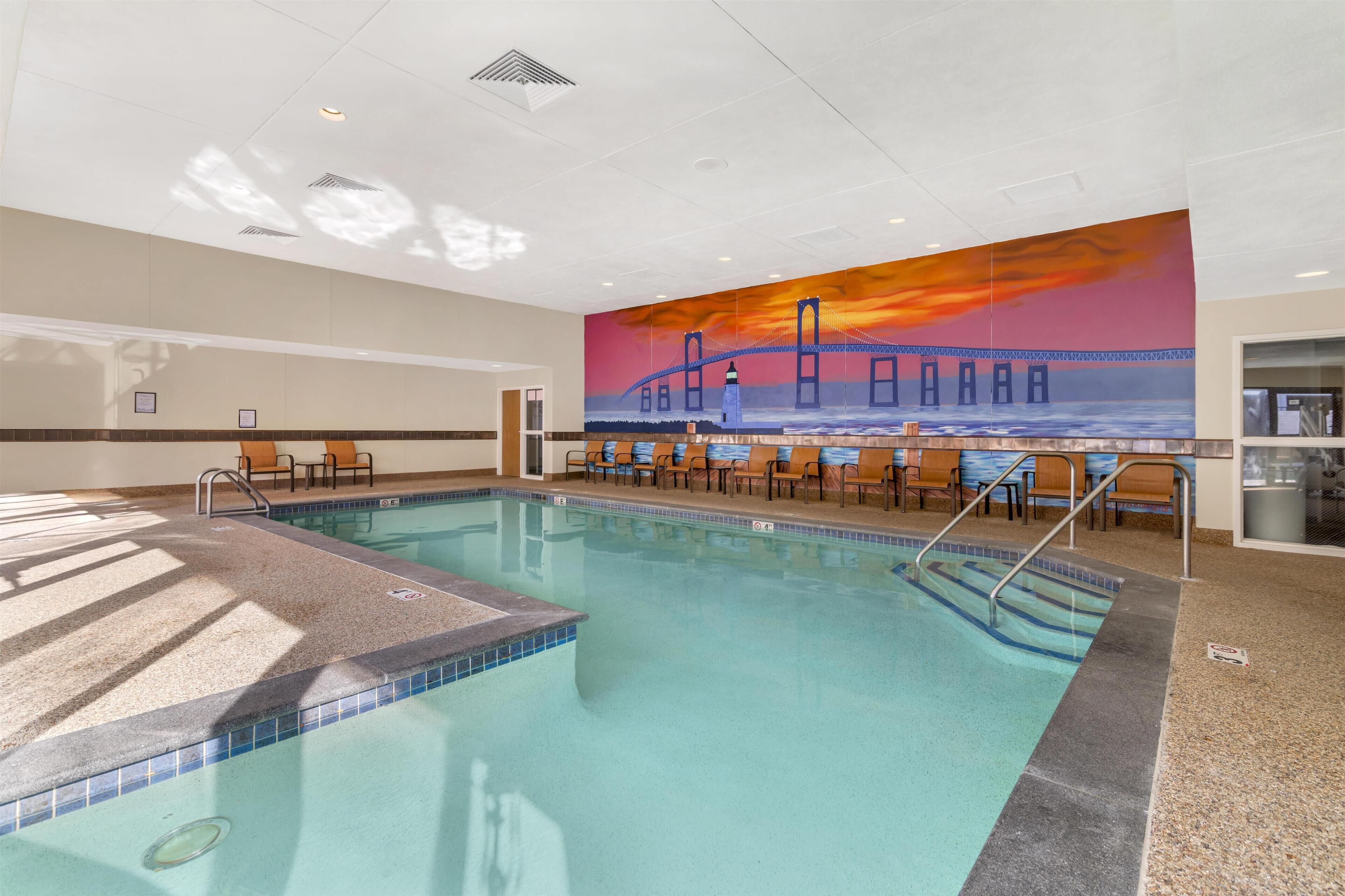 An indoor swimming pool with a sunset mural, lounge chairs, and a tiled deck.