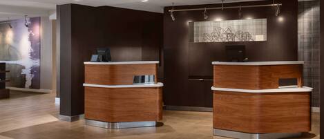 A reception area with two wooden reception desks, a wall-mounted artwork, and a tiled floor.