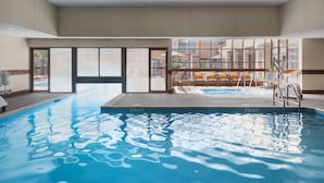 An indoor swimming pool with clear water, a sunlit area with seating, and a view of the outside.