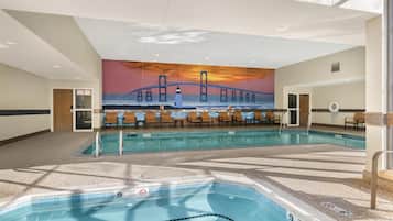 An indoor swimming pool with a mural of a bridge and lighthouse, lounge chairs, and a poolside area.