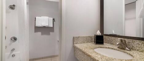 Un baño moderno con lavamanos de granito, un espejo y zona de ducha.