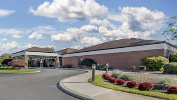 A hotel with a covered entrance, brick exterior, and landscaped garden with red flowers.