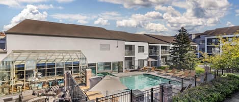 A modern outdoor pool area with a glass-enclosed lounge, seating, and a fire pit.