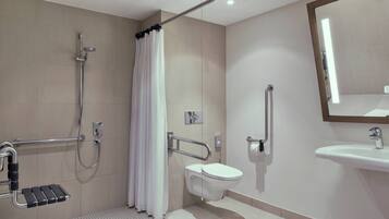 A modern bathroom with a shower, toilet, and sink, equipped with grab bars and a handrail.