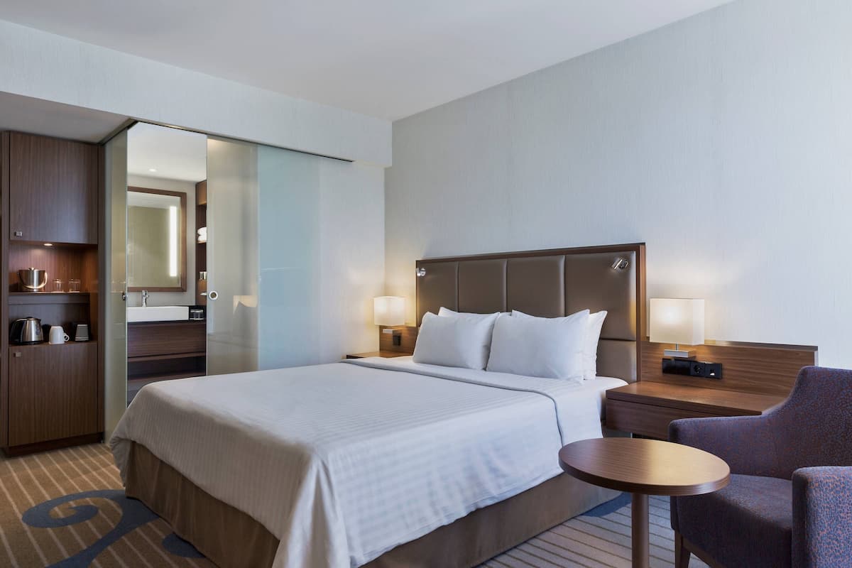 Ein Hotelzimmer mit einem großen Bett, einem Nachttisch mit Lampe, einem Sessel und einem kleinen Tisch.