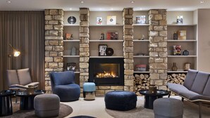 A cozy living room with a stone fireplace, comfortable seating, and a bookshelf filled with books and decorative items. - Courtyard by Marriott Wiesbaden-Nordenstadt (Wiesbaden)