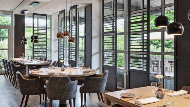 A modern dining area with a round table set for six, surrounded by grey upholstered chairs. - Courtyard by Marriott Wiesbaden-Nordenstadt (Wiesbaden)