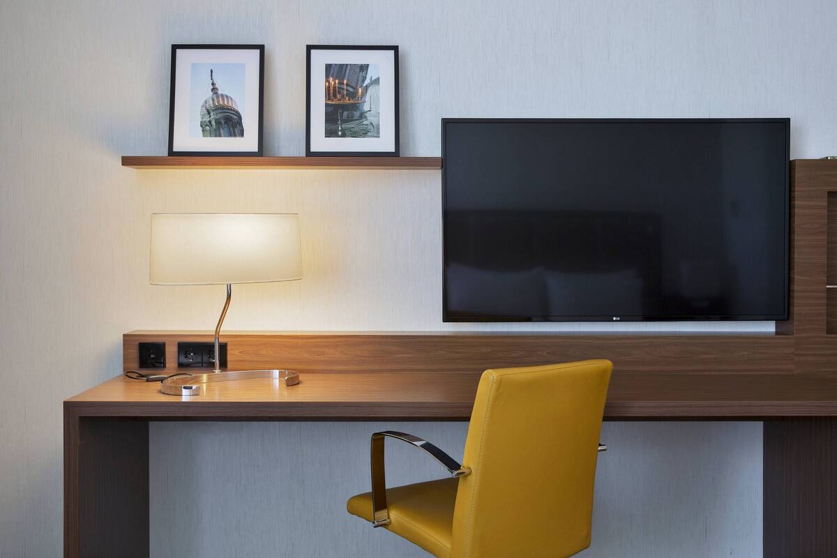 Ein Hotelzimmer mit einem Holztisch, einem Flachbildfernseher, einem gelben Sessel und zwei gerahmten Bildern an der Wand.