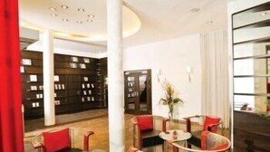 Eine moderne Hotelhalle mit gewölbter Decke, einer zentralen Sitzecke mit runden Tischen und Stühlen sowie einem Bücherregal im Hintergrund.