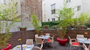 An outdoor dining area with tables and chairs, surrounded by plants and a wooden fence.