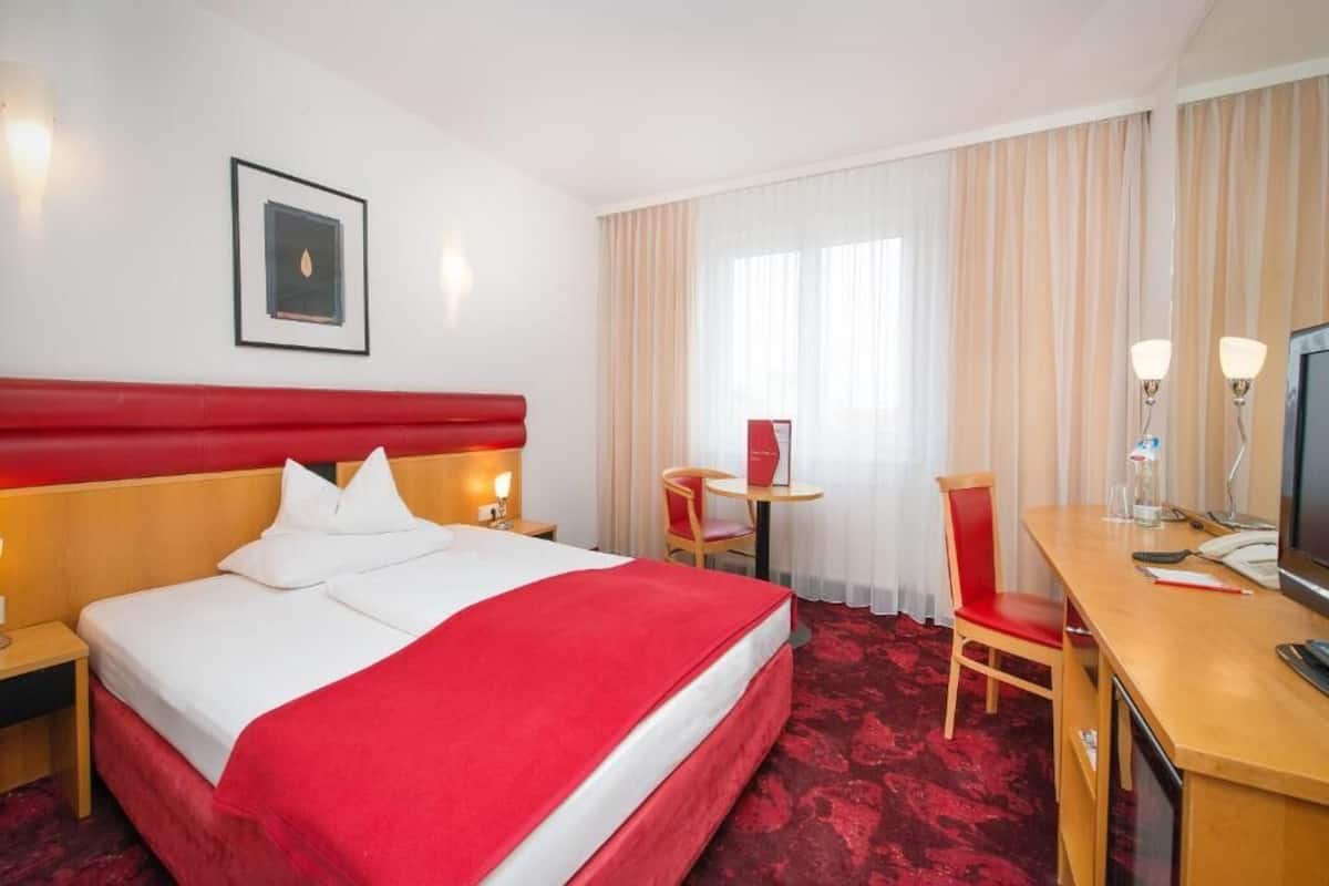 A hotel room with a large bed, a desk, a chair, a television, and a window with curtains.