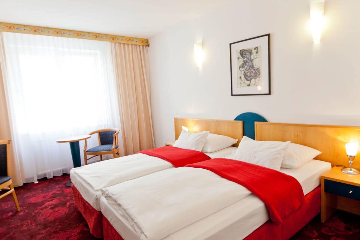 A hotel room with two beds, a chair, a desk, and a painting on the wall.