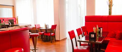 Un restaurante moderno con mobiliario rojo, que incluye una barra y un comedor, con amplias ventanas y un interior limpio y luminoso.