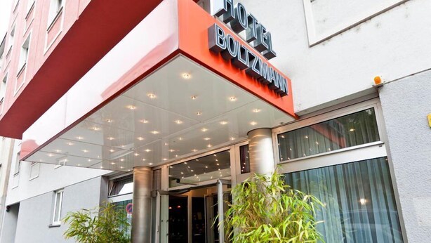 The exterior of Hotel Boltzmann with a modern design, featuring a glass entrance and red potted plants.