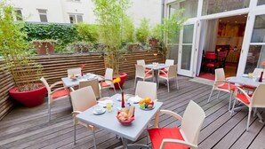 An outdoor patio area with wooden flooring, tables with chairs, and potted plants.