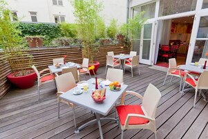 An outdoor patio area with wooden flooring, tables with chairs, and potted plants.