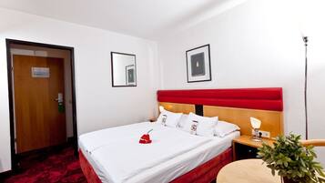 Una habitación de hotel con una cama, una mesita de noche con lámpara, una pequeña mesa y una planta en maceta.