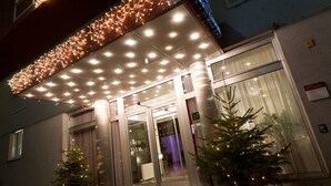 Ein Hotel Eingang mit überdachter Vorfahrt, Glasüren und Weihnachtsbäumen.