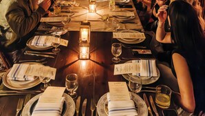 Una larga mesa de comedor preparada para una comida con velas, rodeada de invitados.