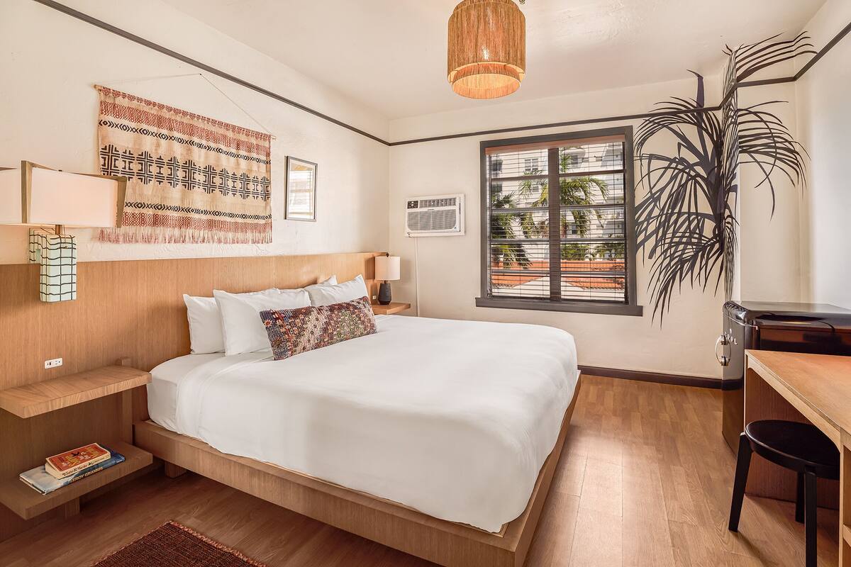A neatly arranged bedroom with a bed, bedside tables, a hanging lamp, a large window, and a potted plant.