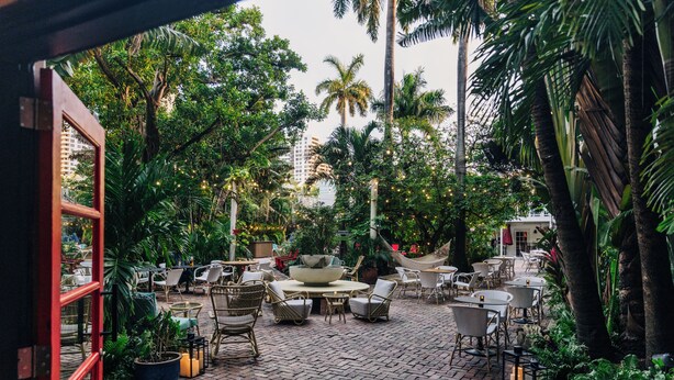 Un patio al aire libre con mobiliario de mimbre, plantas en macetas y suelo de ladrillo.