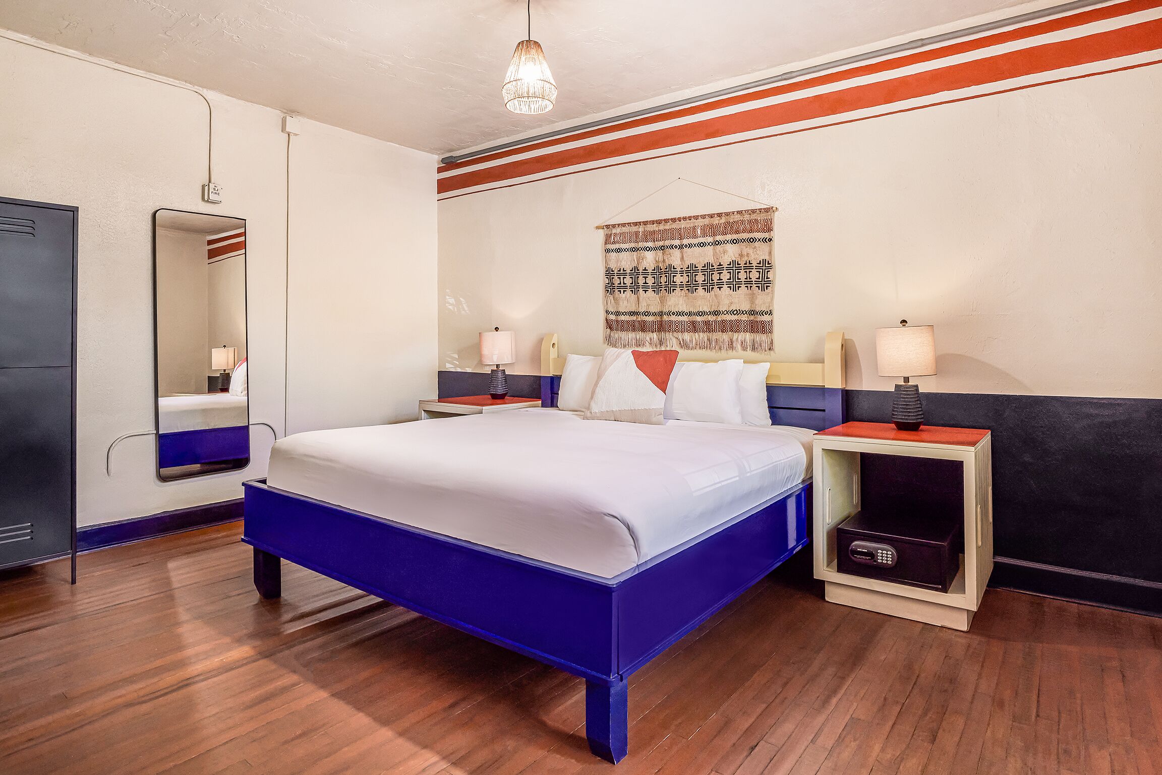 Ein Hotelzimmer mit einem großen Bett, Nachttischen, einem Spiegel und einem Wandteppich.