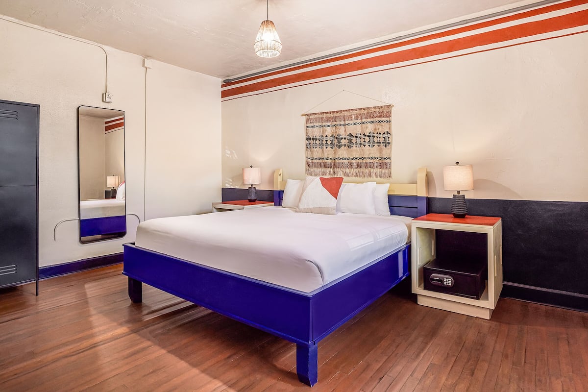Habitación de hotel con una cama grande, mesitas de noche, un espejo y un tapiz en la pared.