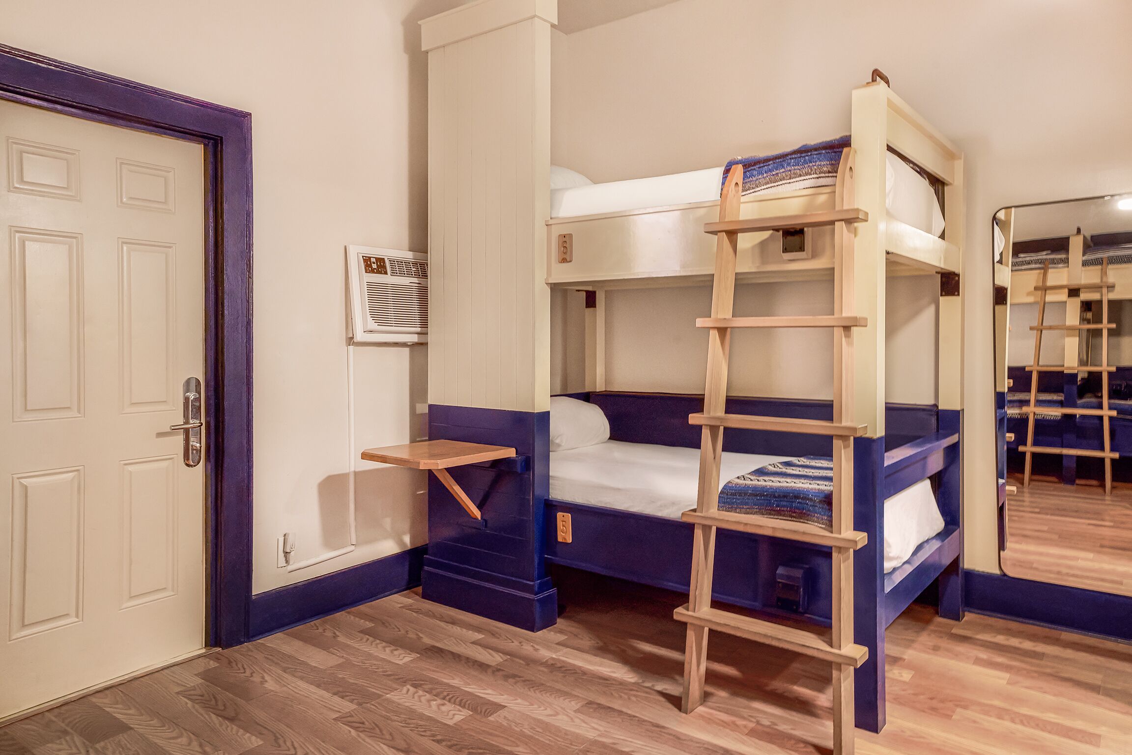 Une chambre avec un lit superposé, une échelle en bois, une petite étagère et une porte.