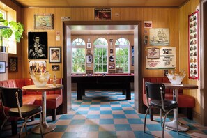 A pool table in a room with wooden walls, red leather booths, and a checkered floor.