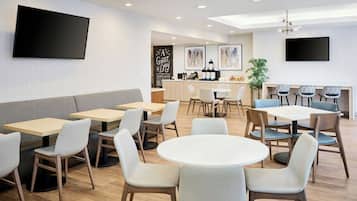 A modern dining area with tables and chairs, a bar area with a counter and seating, and a flat-screen TV mounted on the wall.