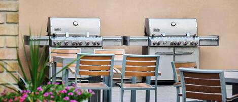 Two Weber Summit gas grills with multiple burners, set up outdoors with tables and chairs.