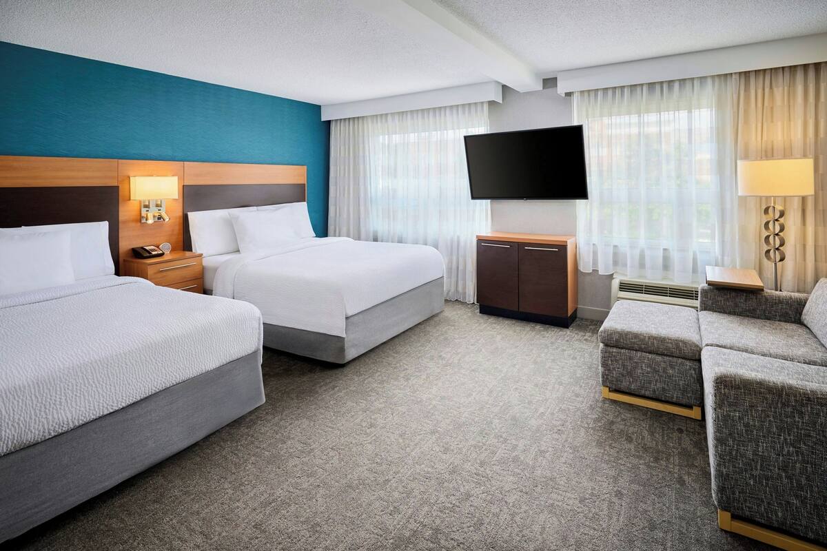 Une chambre d’hôtel avec deux lits, un bureau, un téléviseur à écran plat, une lampe et un canapé.